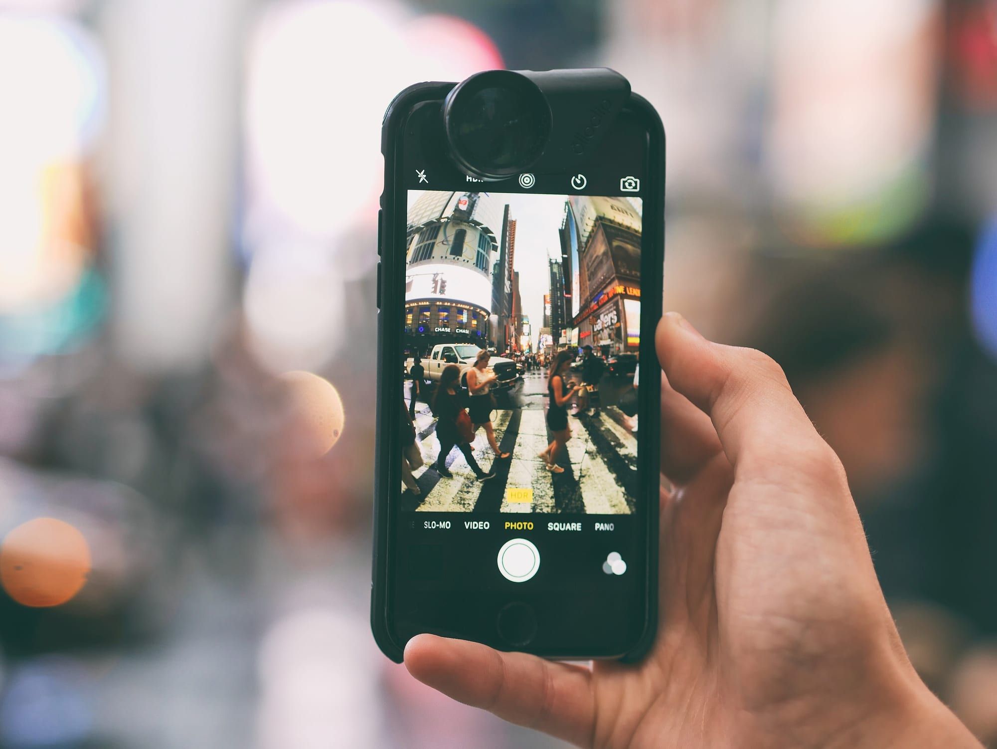 A hand holding a smartphone, photographing a busy city street on its screen