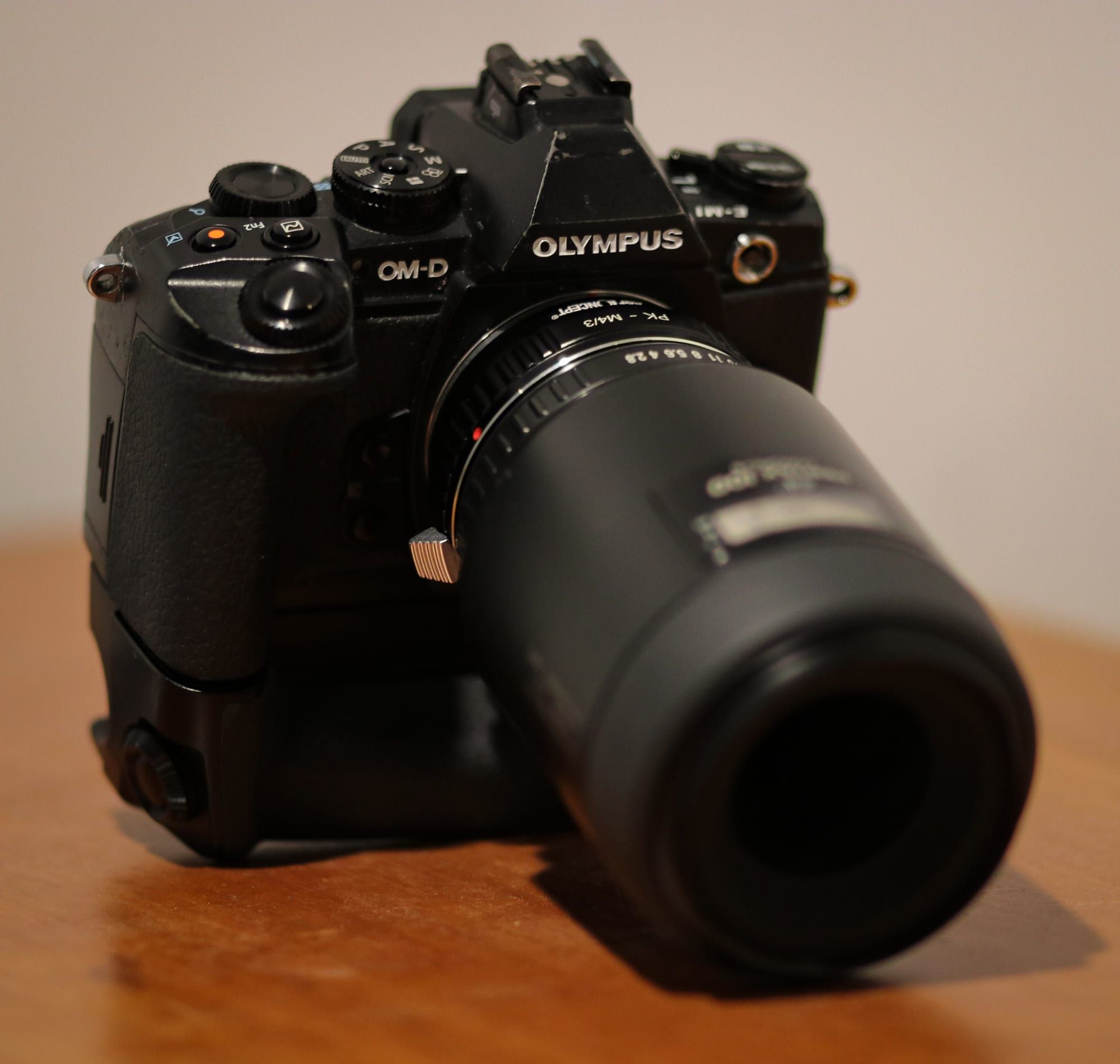 An Olympus OM-D E-M1 mirrorless camera body with an adapted lens resting on a wooden table